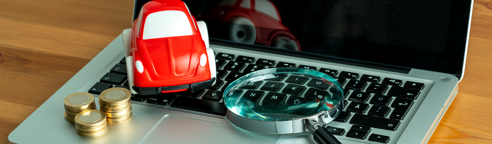 Lupa, model samochodu i stos monet leżące na laptopie